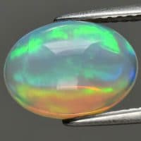 Natural gemstone opal in tongs on background