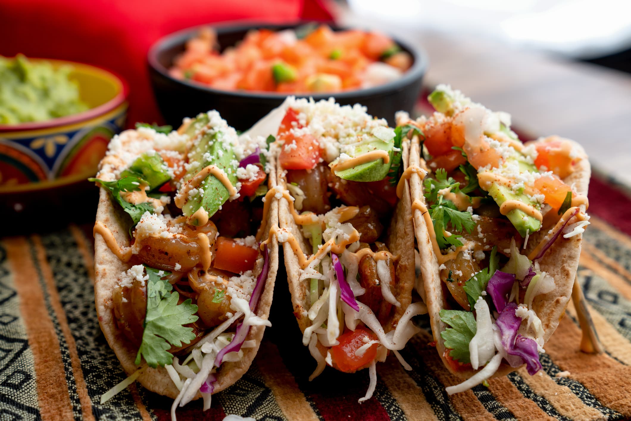 A beautiful arrangement of shrimp tacos with pico de gallo, avocado, cilantro, chipotle sour cream, and cotija cheese