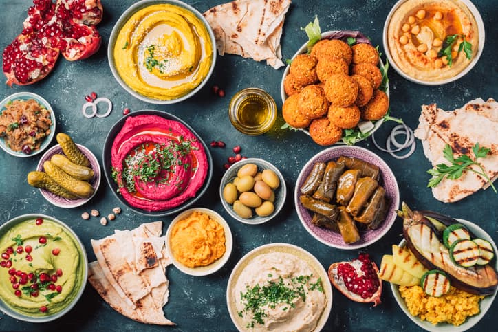 Arabic traditional cuisine. Middle Eastern meze with pita, olives, colorful hummus, falafel, stuffed dolma, babaganush, pickles, vegetables, pomegranate, eggplants. Mediterranean appetizer party idea.