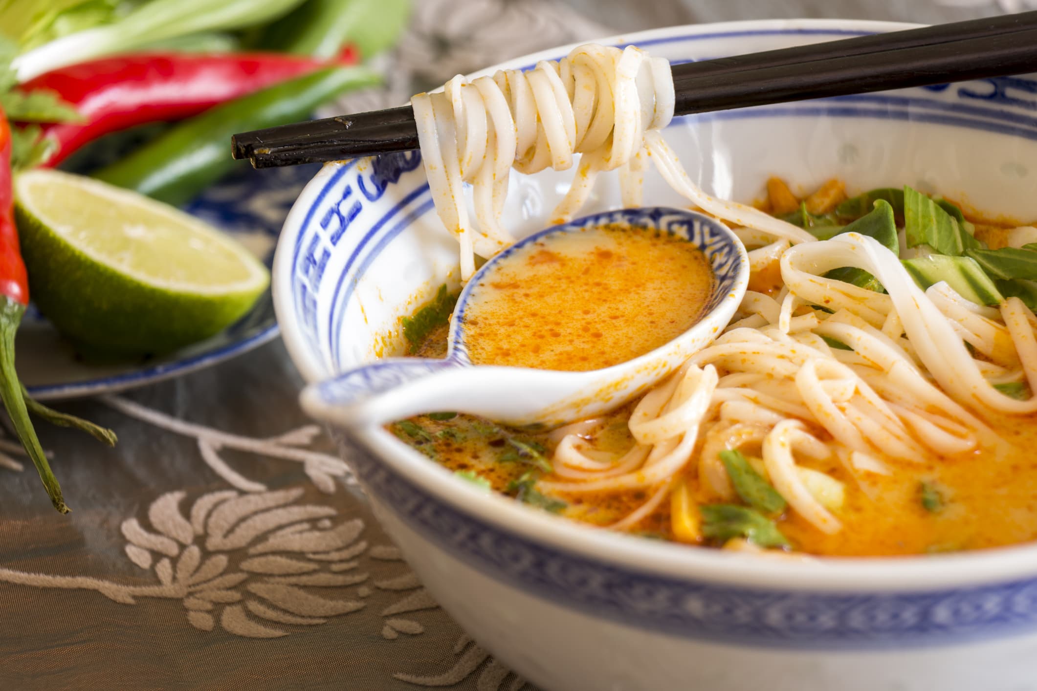 Bowl of spicy Asian soup with noodles and vegetables for a delicious appetizer served with chopsticks and surrounded by fresh ingredients