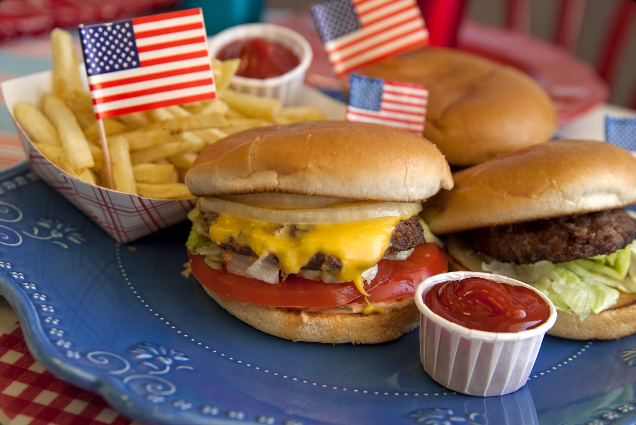 "American Fourth of July, Memorial &amp; Labor Day barbeque hamburgers, cheeseburgers &amp; french fries on picnic lunch table &amp; patriotic flags. (SEE LIGHTBOXES BELOW for more grilled summer food...)"