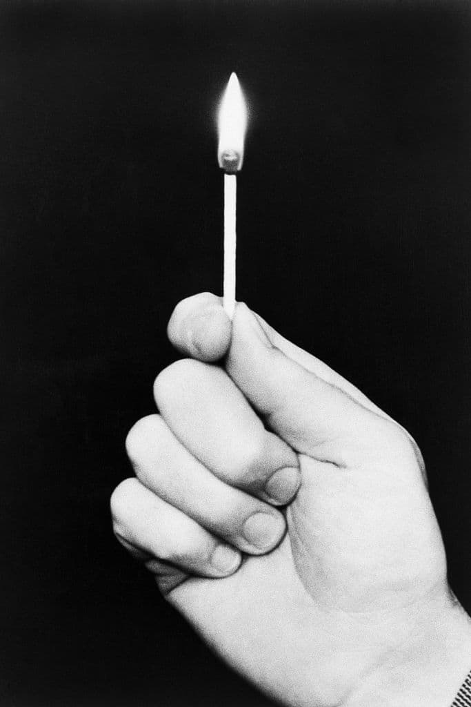 (Original Caption) Photo shows a hand holding a lit match on a black background. Undated.