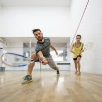 Low angle view of young couple exercising racketball on a court. Focus is on man reaching for the ball.