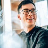 Portrait of a young handsome Asian entrepreneur wearing smart glasses, smiling and looking forward to his future startup innovations. New business owners and technology moving forward