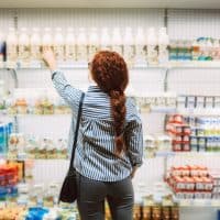 Young woman in striped shirt from back choosing dairy products in modern supermarket