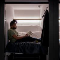 Young adult male reading in a capsule hotel. Tokyo, Japan. March 2018
