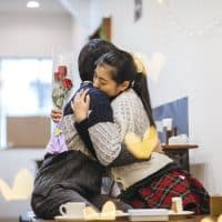 A Japanese girlfriend is happily hugging her boyfriend with flowers in her hand.
