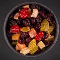 Mix variety of dried fruit in bowl over black dark stone background