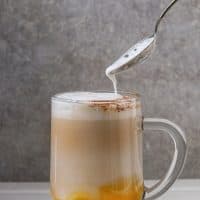 Glass of pumpkin layered spice latte with pumpkin puree. milk foam flowing from spoon and cinnamon standing on white marble table with grey wall at background. Copy space. (Photo by: Natasha Breen/REDA&amp;CO/Universal Images Group via Getty Images)