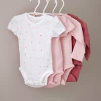 Set of children bodysuits pastel colored on clothes hangers.