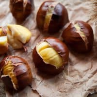Traditional Christmas dish  - Ripe Sweet Roasted Chestnuts, cracked shells after put to the fire, natural paper and old wooden rustic background.