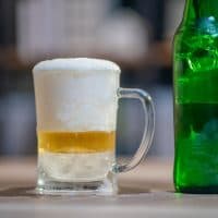 Ice cold glass of beer with overflowing foam and  green bottle.