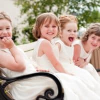 Color photo of four happy little flower girls laughing together while wearing formal dresses. They are sisters and cousins.