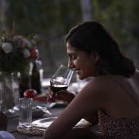 Smiling young woman having red wine sitting by friend at table in party during sunset