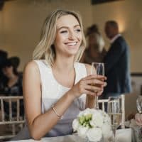 Young woman is sitting at a table at a wedding with a glass of champagne.