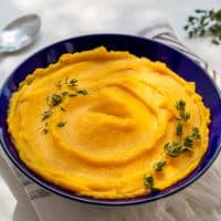 Autumn pumpkin puree in bowl. Autumnal pumpkin cream soup with thyme on white table. Autumn tasty vegetarian food. Top view