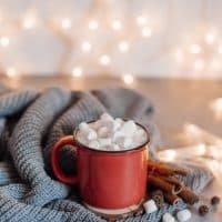 Christmas cocoa header with marshmallows, chocolate crumbs, and syrup. Large coffee cup with homemade hot chocolate. Winter drink photography on a dark background.