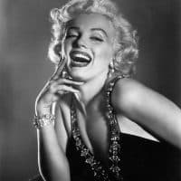 circa 1952:  Half-length portrait of American actor Marilyn Monroe (1926  - 1962) laughing, her hand raised to her cheek, wearing a low cut dress trimmed in jewels.  (Photo by Hulton Archive/Getty Images)