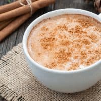 white cup of salep milky traditional hot drink of Turkey with cinnamon powder and sticks on rustic vintage wooden table. Sahlep background