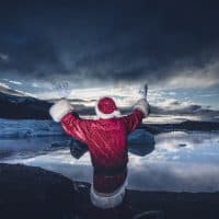Iceland, rear view of a man disguised as Santa Claus standing at a glacier raising his arms