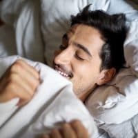 Smiling young man sleeping comfortably in bed at home