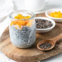 Chia pudding in glass jar with almond milk and mango on wooden cut board, white background - healthy superfood vegan, dairy free breakfast