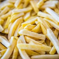 Macro closeup of frozen uncooked raw straight cut salty french fries pommes frites on oven baking tray before cooking or frying with texture detail
