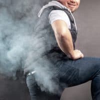 Man lift the leg and fart in front of grey background