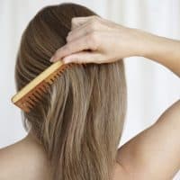 Woman combing hair with natural wooden comb, caring for herself in a natural and organic way